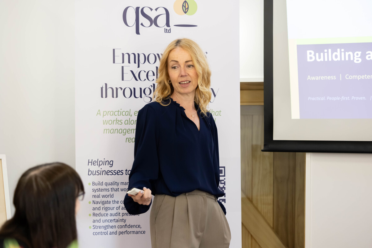 Charlotte presenting to a rrom of people in front of a roller banner and projector screen