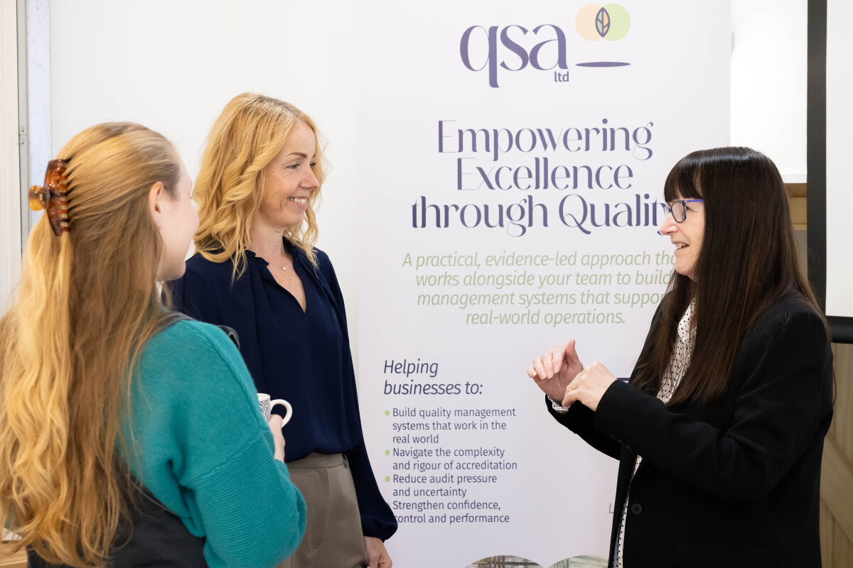Carol and Charlotte having a conversation with a lady in front of a QSA branded roller banner