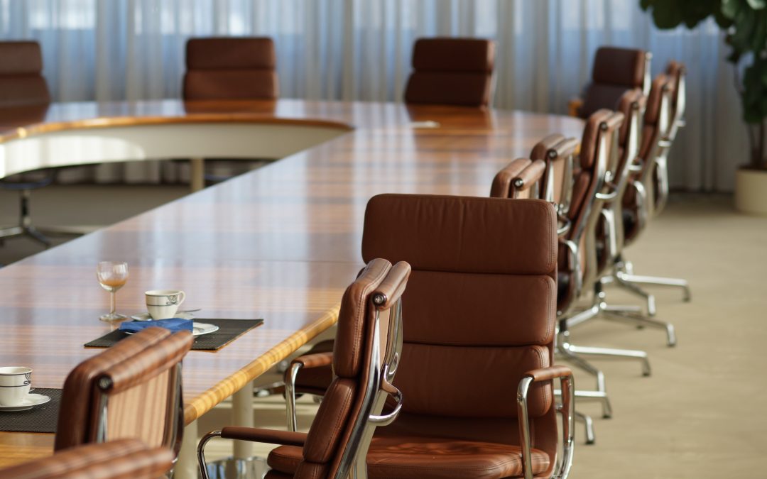 Empty brown leather office chairs around a table in a large corporate boardroom.