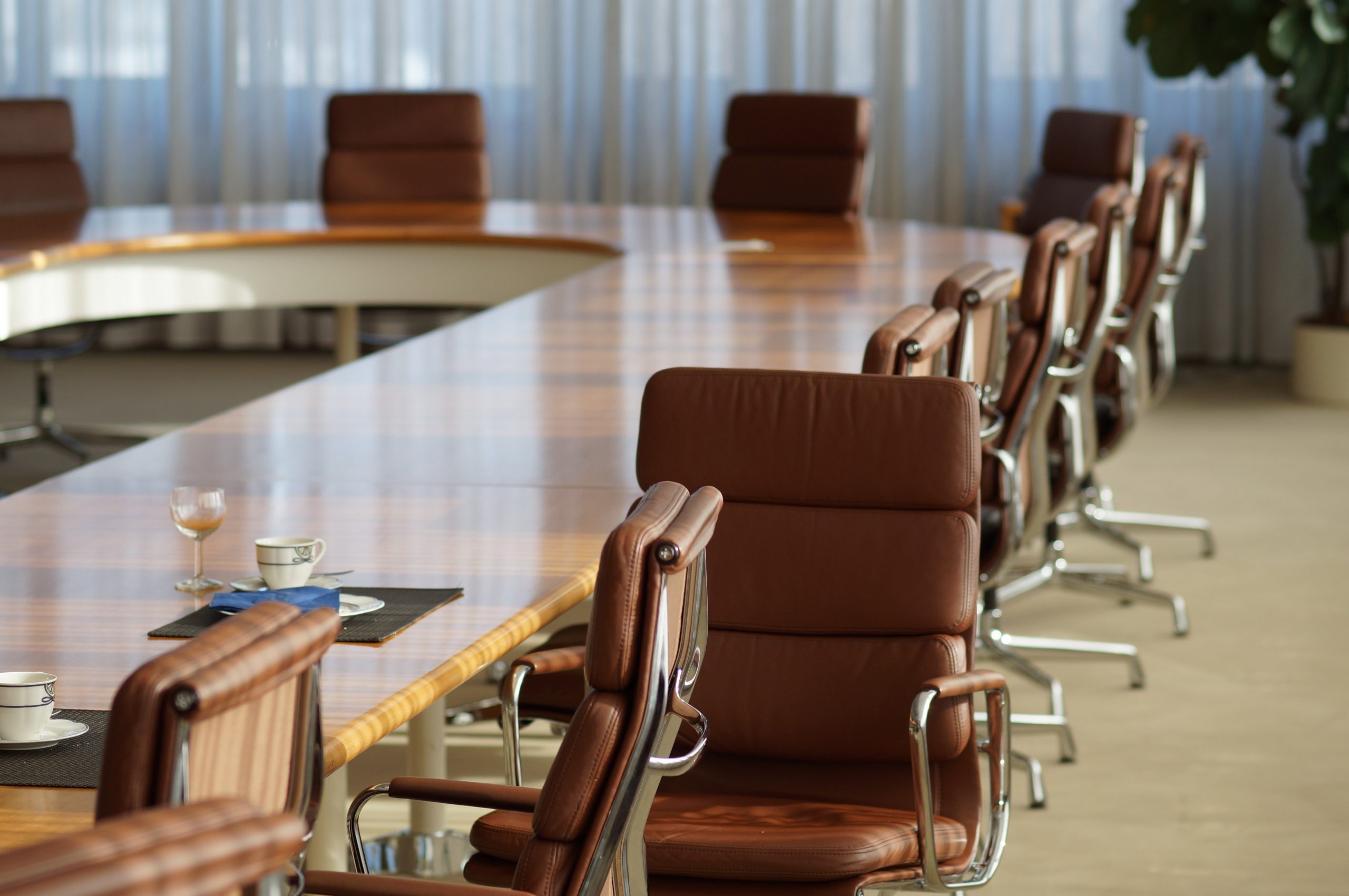 Empty brown leather office chairs around a table in a large corporate boardroom.