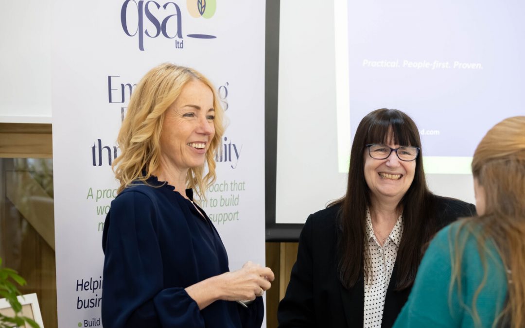 Charlotte of QSA having a conversation with peers whilst standing in front of a QSA roller banner display