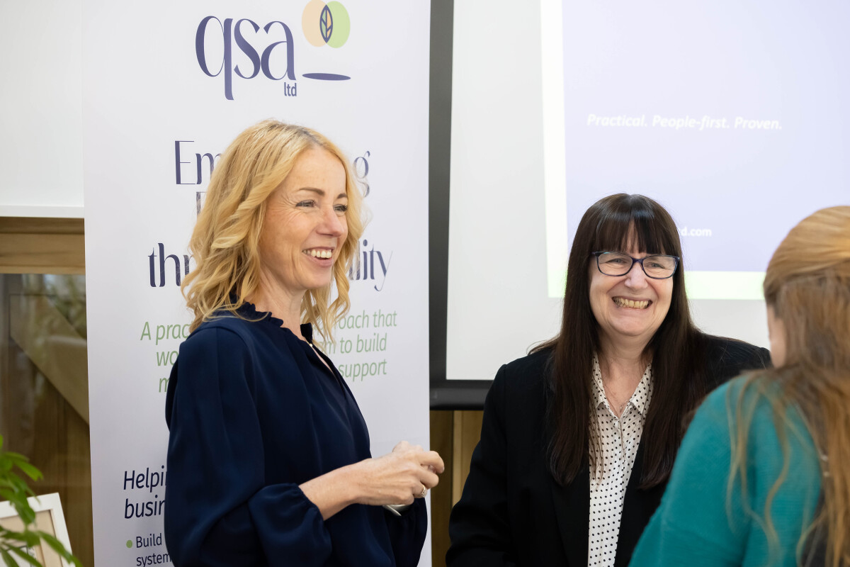 Charlotte of QSA having a conversation with peers whilst standing in front of a QSA roller banner display